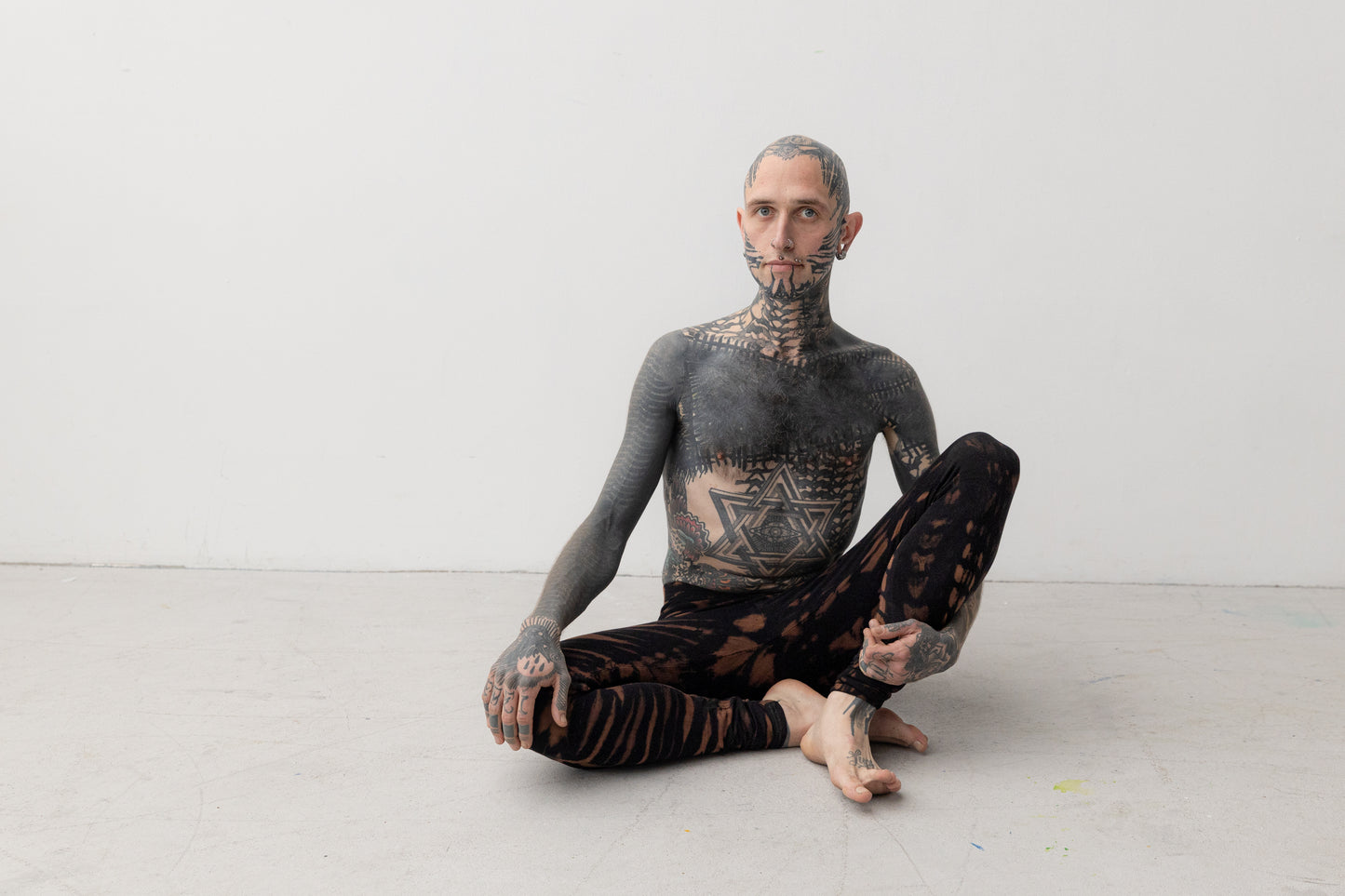 Mann sitzend trägt bequeme Batik Animal Print Leggings türkis-braun – Unisex Yoga Pants im alternativen Psytrance Look Tie-Dye