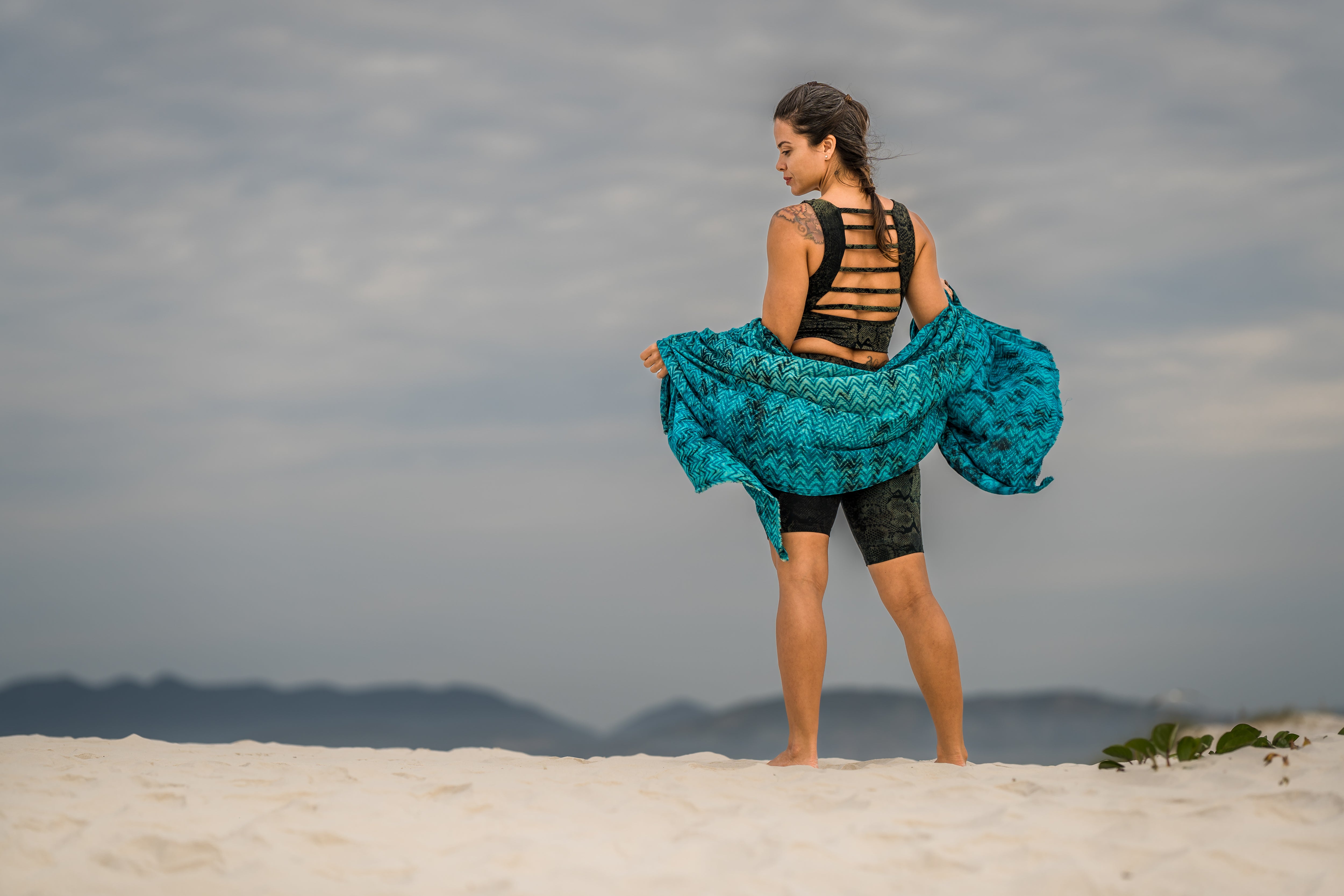 Rückansicht eines Models mit blau-grün-braunem Viskose-Sarong im Wellen-Batikmuster, lässig über Rücken und Arme drapiert