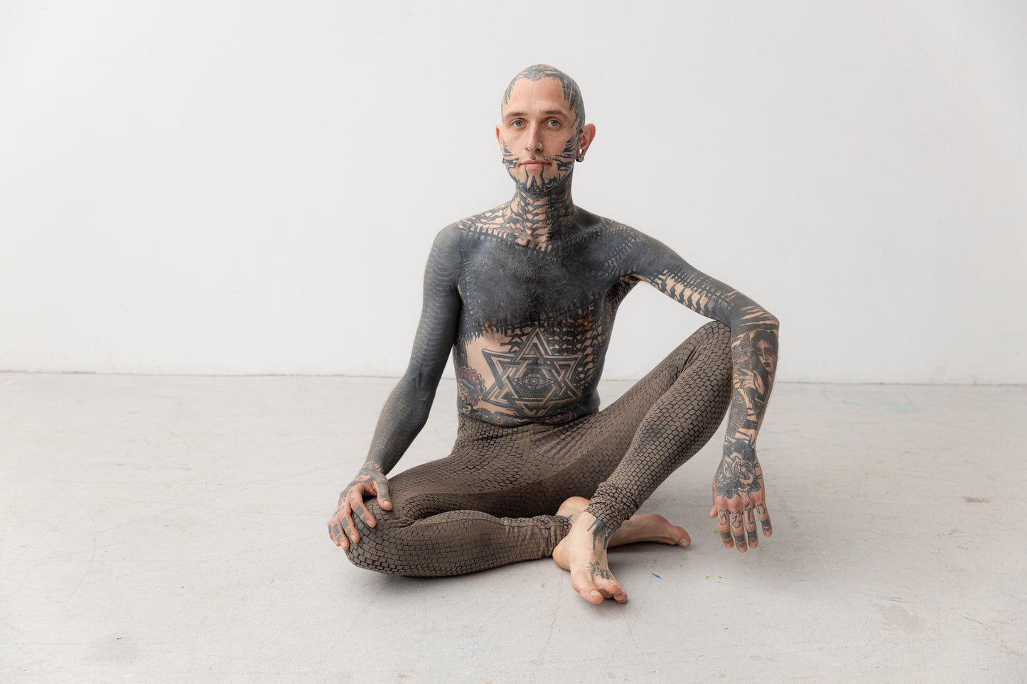Männlich gelesenes Model trägt ausgefallene Leggings mit künstlerisch ungleichmäßigem Druck. Aufnahme im Sitzen.