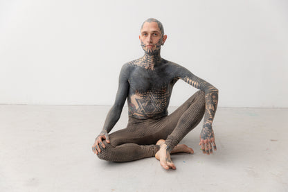 Männlich gelesenes Model trägt ausgefallene Leggings mit künstlerisch ungleichmäßigem Druck. Aufnahme im Sitzen.