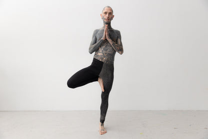 Yoga Pose von männlich gelesenem Model, das Leggings mit asymmetrischem Print trägt.