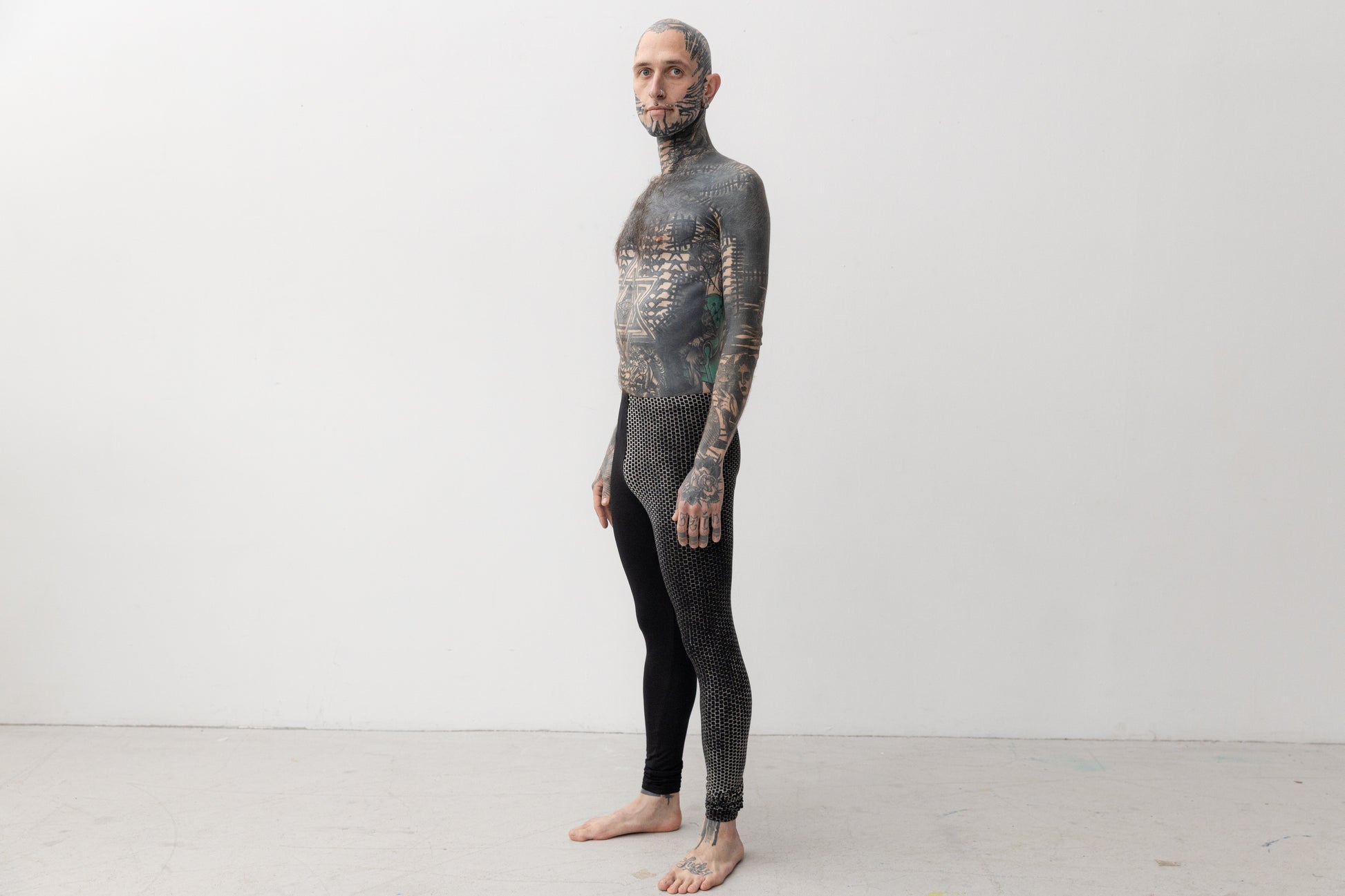 Tätowiertes Model trägt genderneutrale Leggings mit asymmetrischem Print an einem Bein.