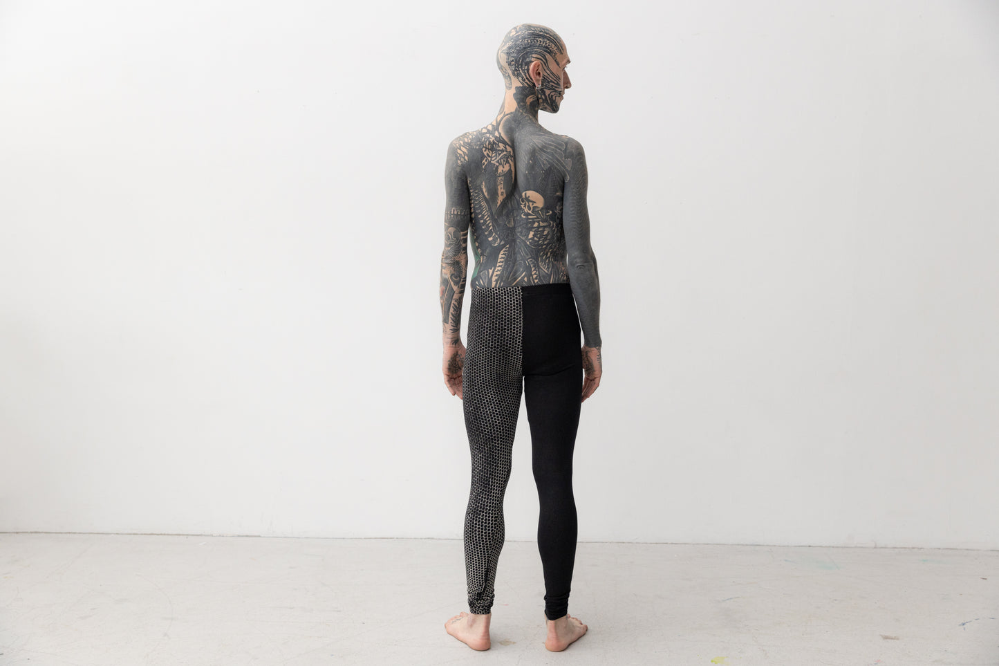 Männlich gelesenes Model trägt Leggings mit asymmetrischem Print an einem Bein, Aufnahme von hinten.
