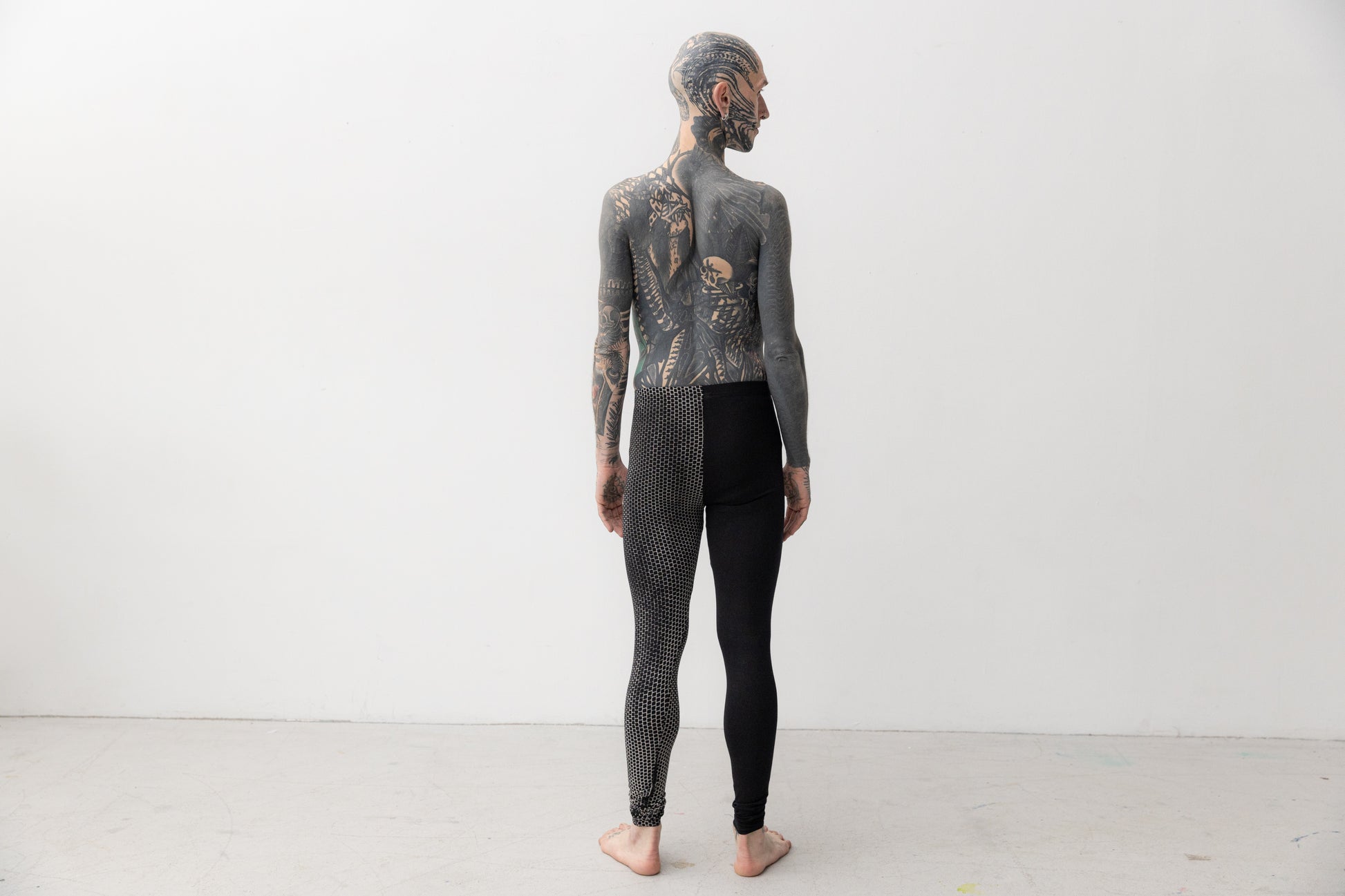 Männlich gelesenes Model trägt Leggings mit asymmetrischem Print an einem Bein, Aufnahme von hinten.