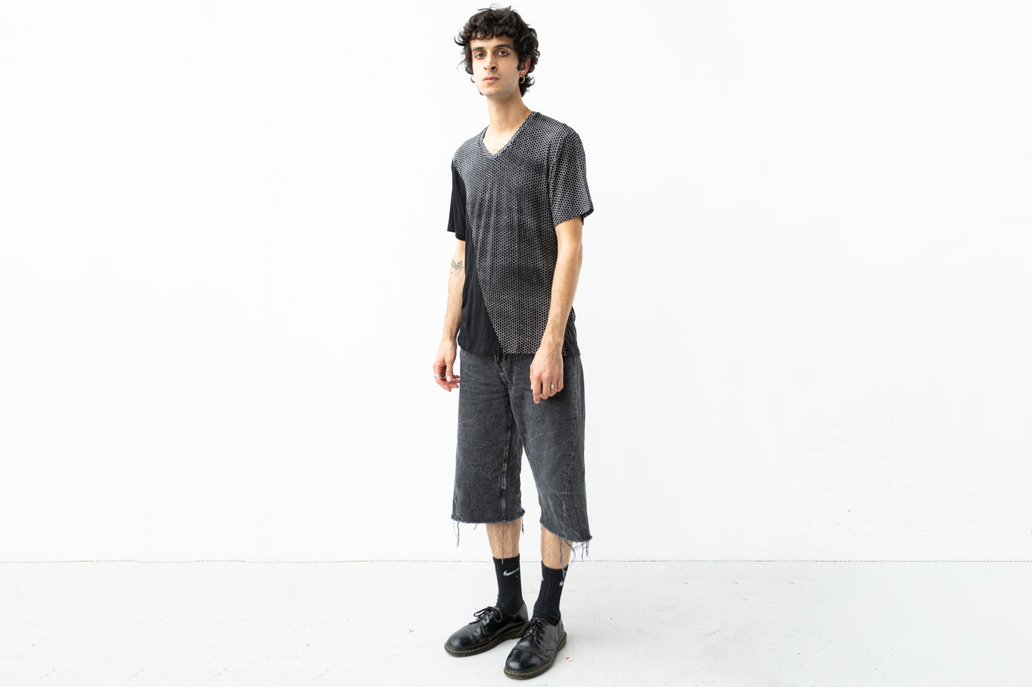 Männlich gelesenes Model trägt asymmetrisch bedrucktes T-Shirt mit Hexagon-Muster.