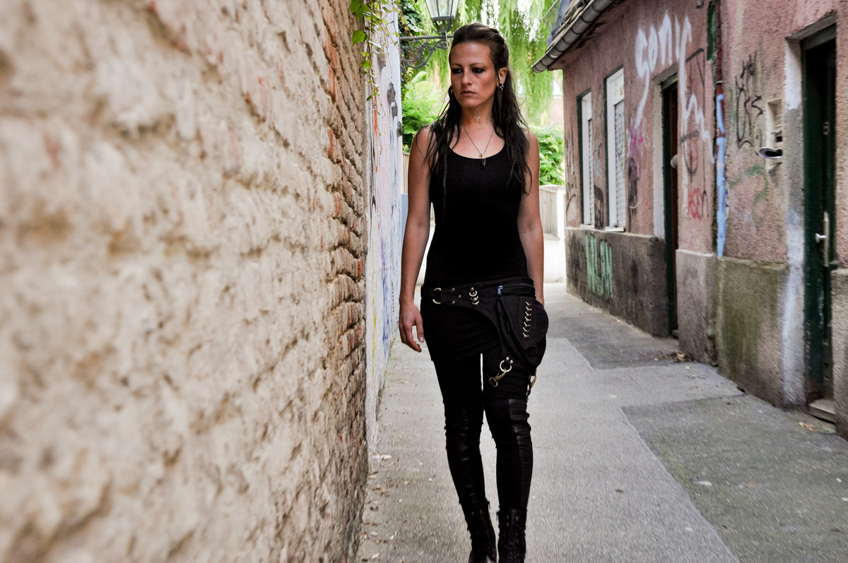 Alternative Frau trägt schwarze Bauchtasche mit Beinschnalle in einer Gasse, Ganzkörperansicht im Gehen