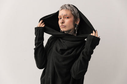 Oberkörperaufnahme eines ausdrucksstarken Models, das eine Kapuze eines oversized schwarzen Cardigans hält