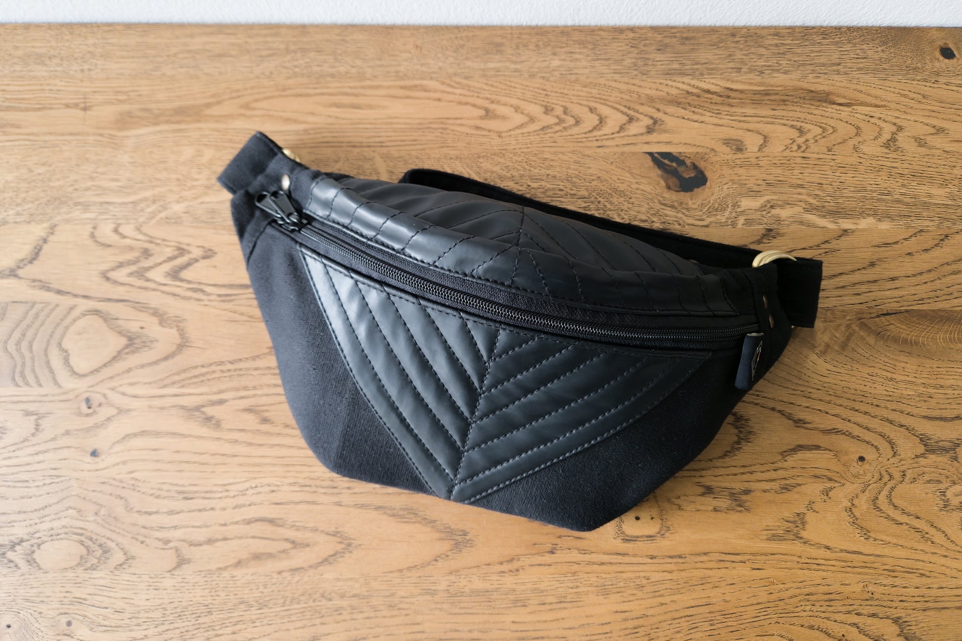 Crossbody-Tasche mit Reißverschluss und Messingbeschlägen, liegend auf Tisch.