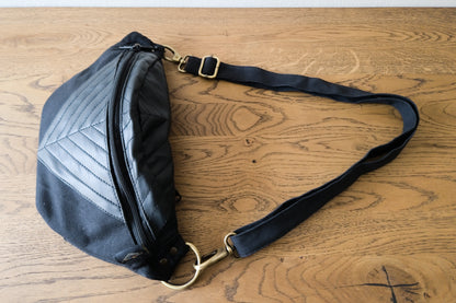 Crossbody-Tasche aus Baumwolle mit Kunstlederapplikation in schwarz, Gesamtansicht liegend, große Größenvariante L-XL-XXL mit Riemen der an der Enden mit messingfarbenen Karabinerhaken an der Tasche befestigt ist.