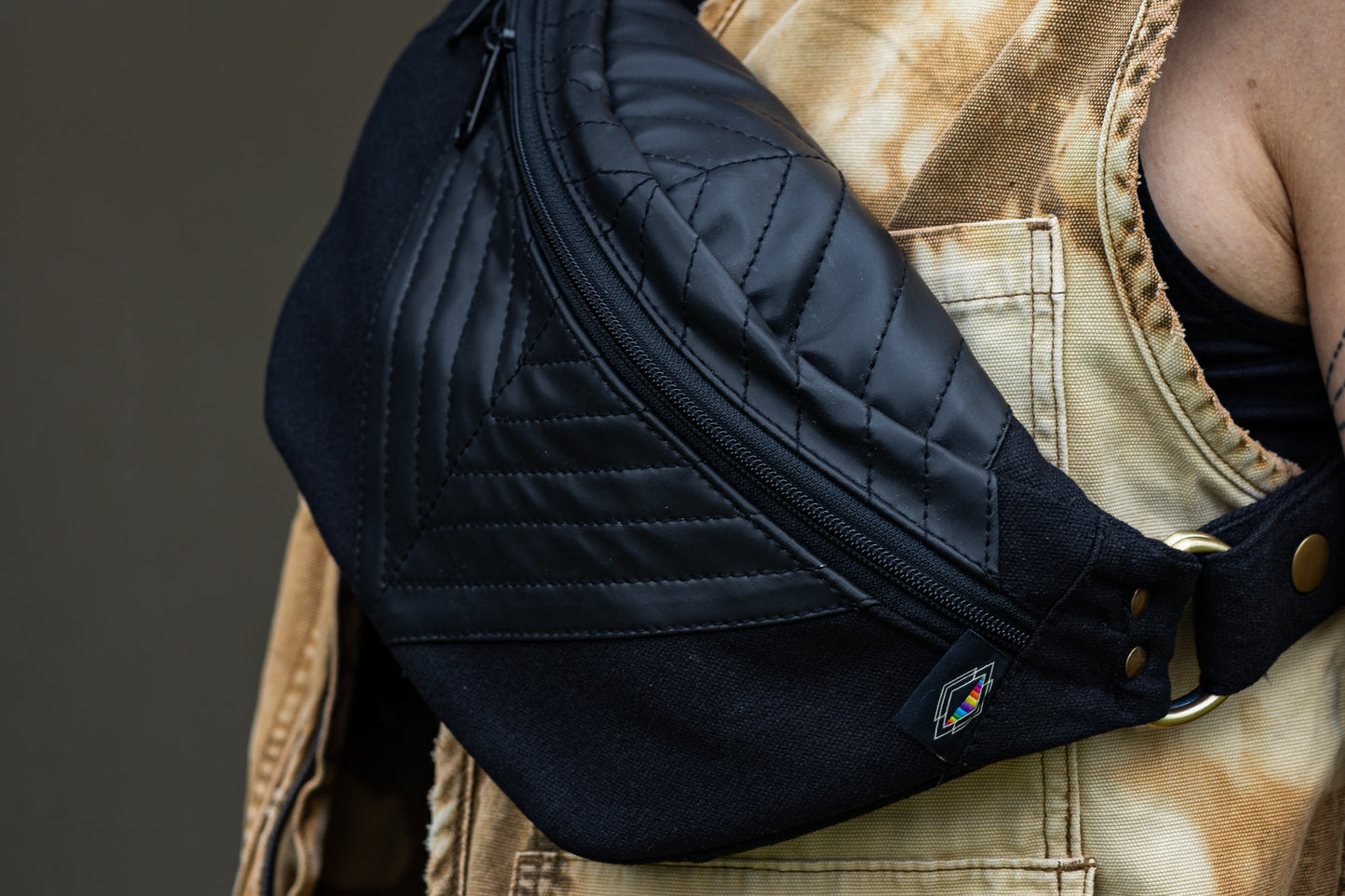 Nahaufnahme von schwarzer Bauchtasche mit Kunstleder und dekorativer Nahtstruktur, getragen über der Brust.