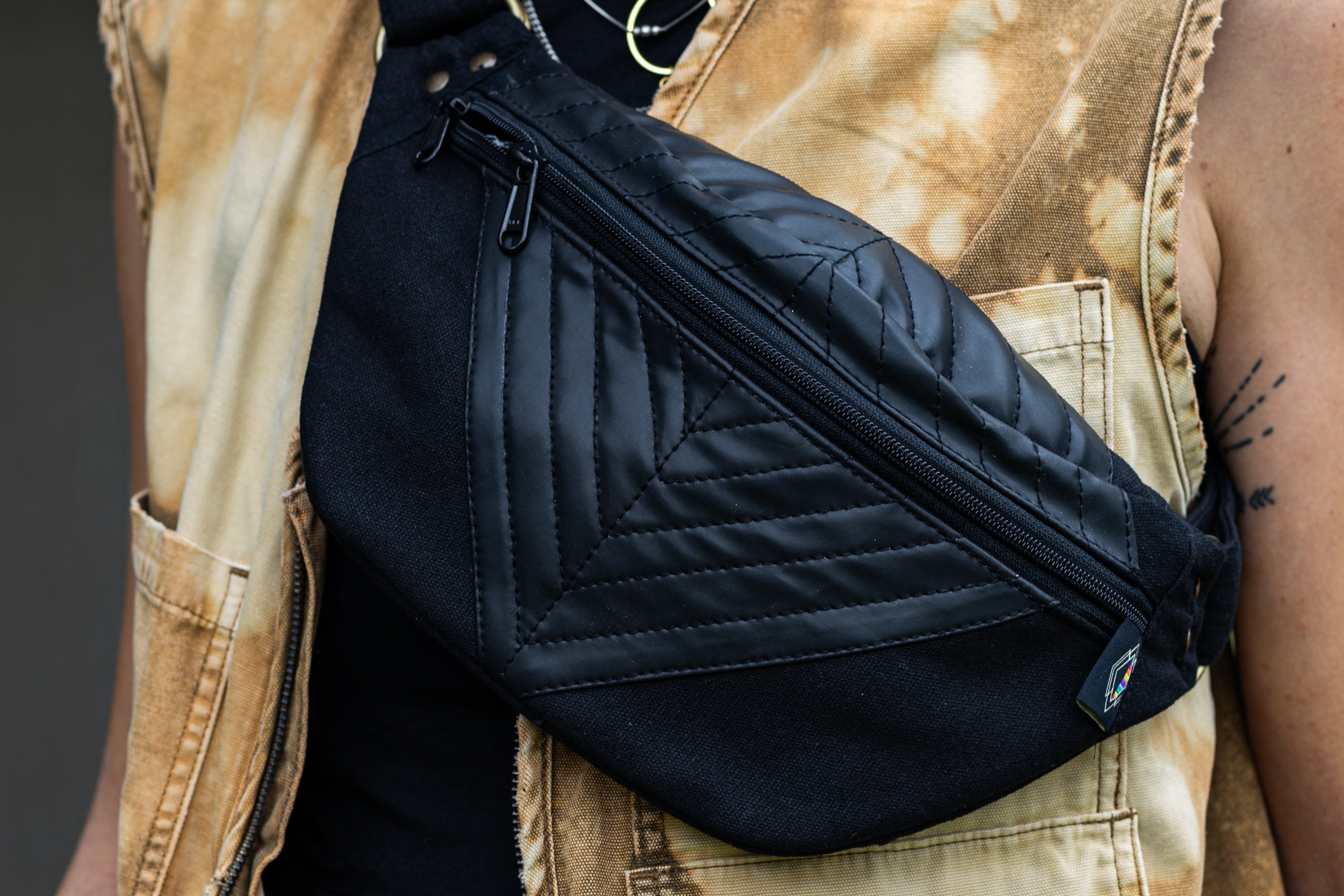 Nahaufnahme von schwarzer Crossbody-Tasche mit Kunstleder und geometrischer Nahtstruktur, getragen über der Brust.