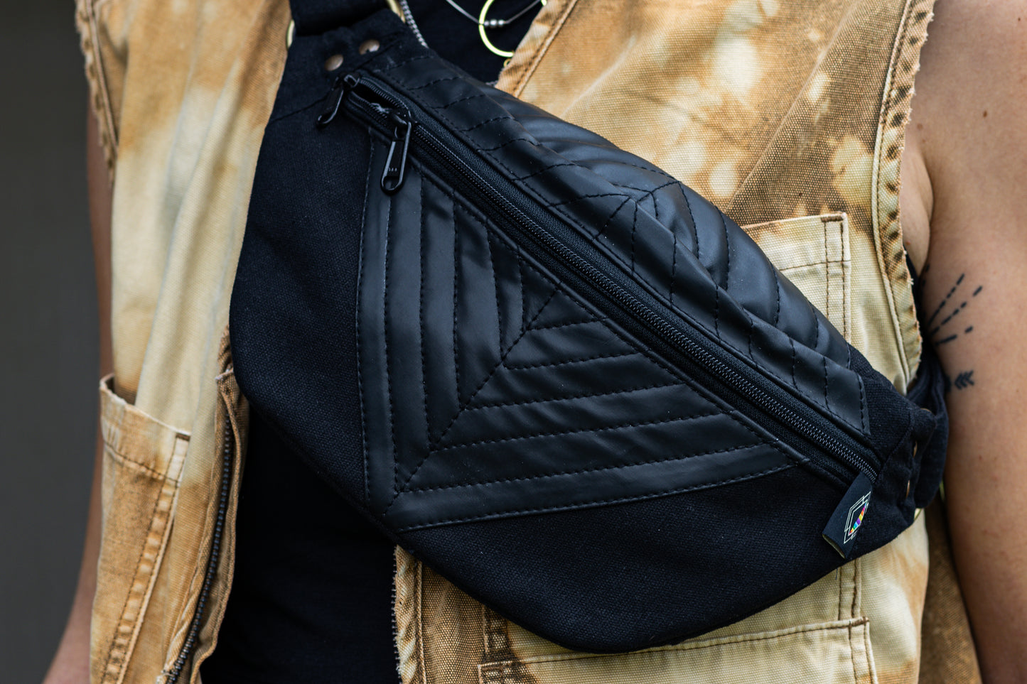 Nahaufnahme von schwarzer Crossbody-Tasche mit Kunstleder und geometrischer Nahtstruktur, getragen über der Brust.