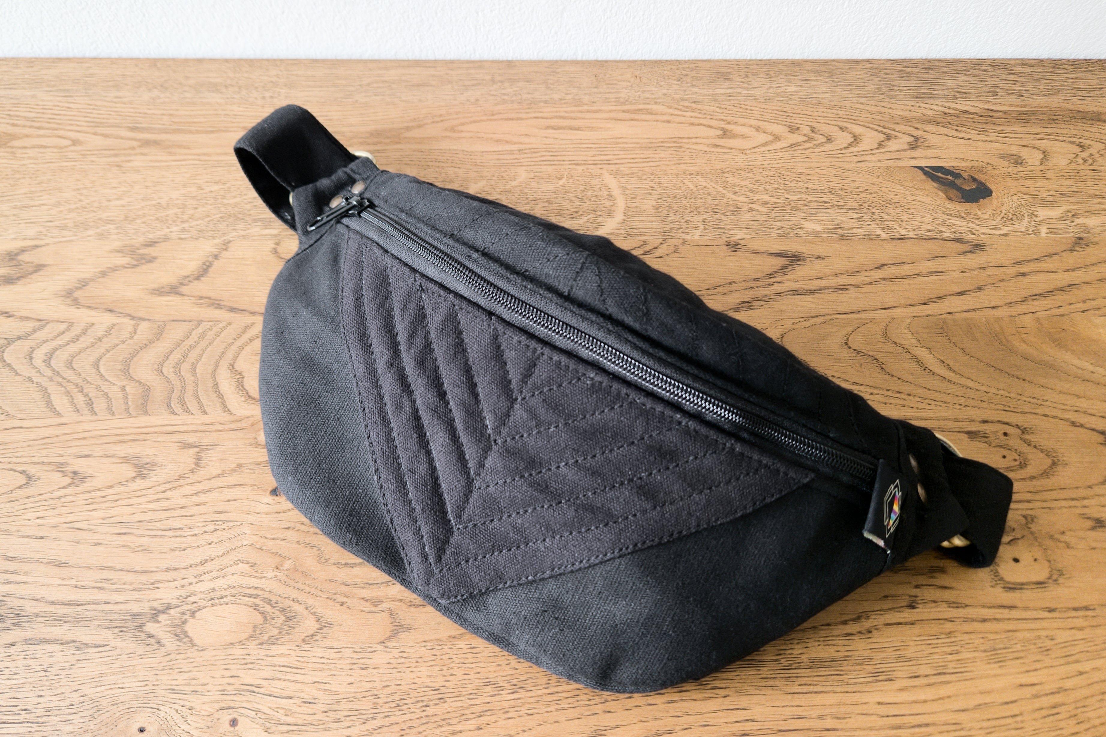 Crossbody-Tasche mit Reißverschluss und Messingbeschlägen, liegend auf Tisch.