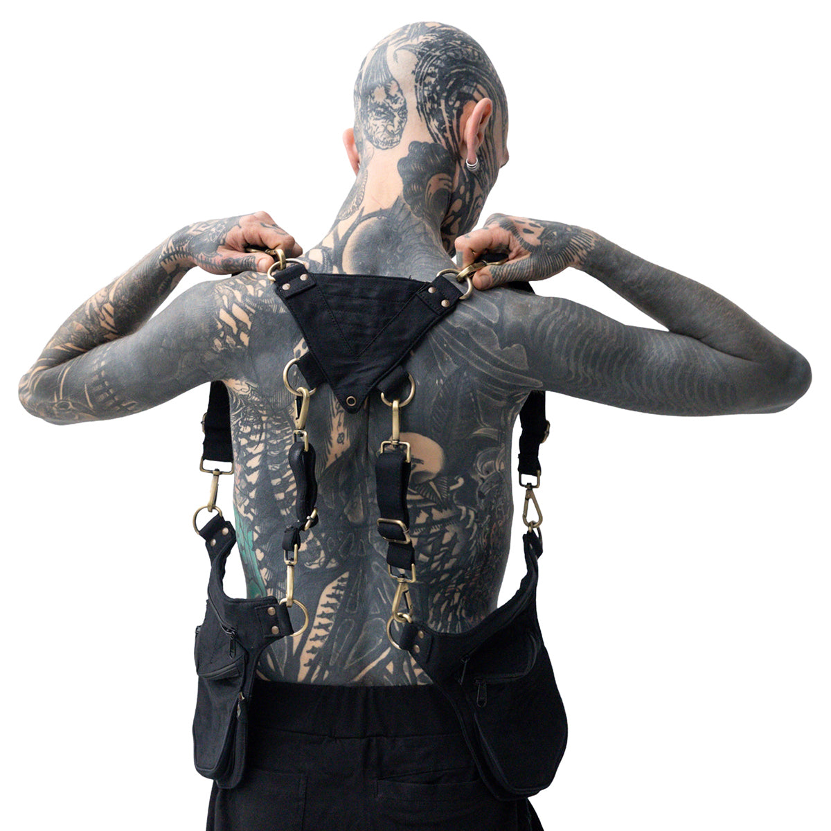 Oberkörperfreies, tätowiertes Model von hinten trägt eine doppelte Canvas-Schultertasche im Harness-Stil