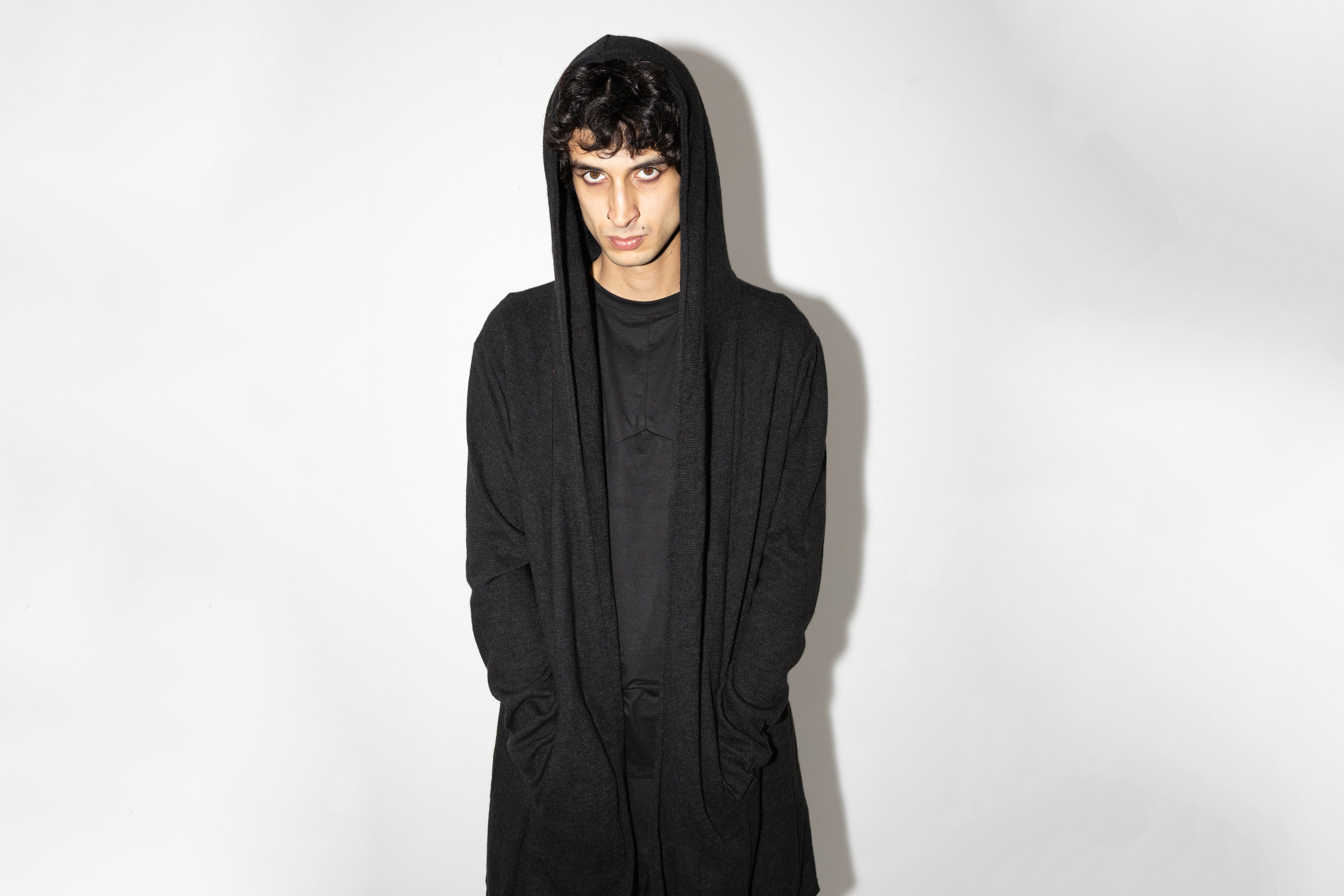 Nahaufnahme von Model, das schwarzen genderneutralen Strickmantel mit Kapuze trägt, im Cyberpunk-Stil.