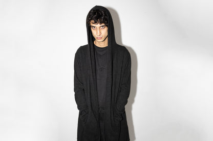 Nahaufnahme von Model, das schwarzen genderneutralen Strickmantel mit Kapuze trägt, im Cyberpunk-Stil.