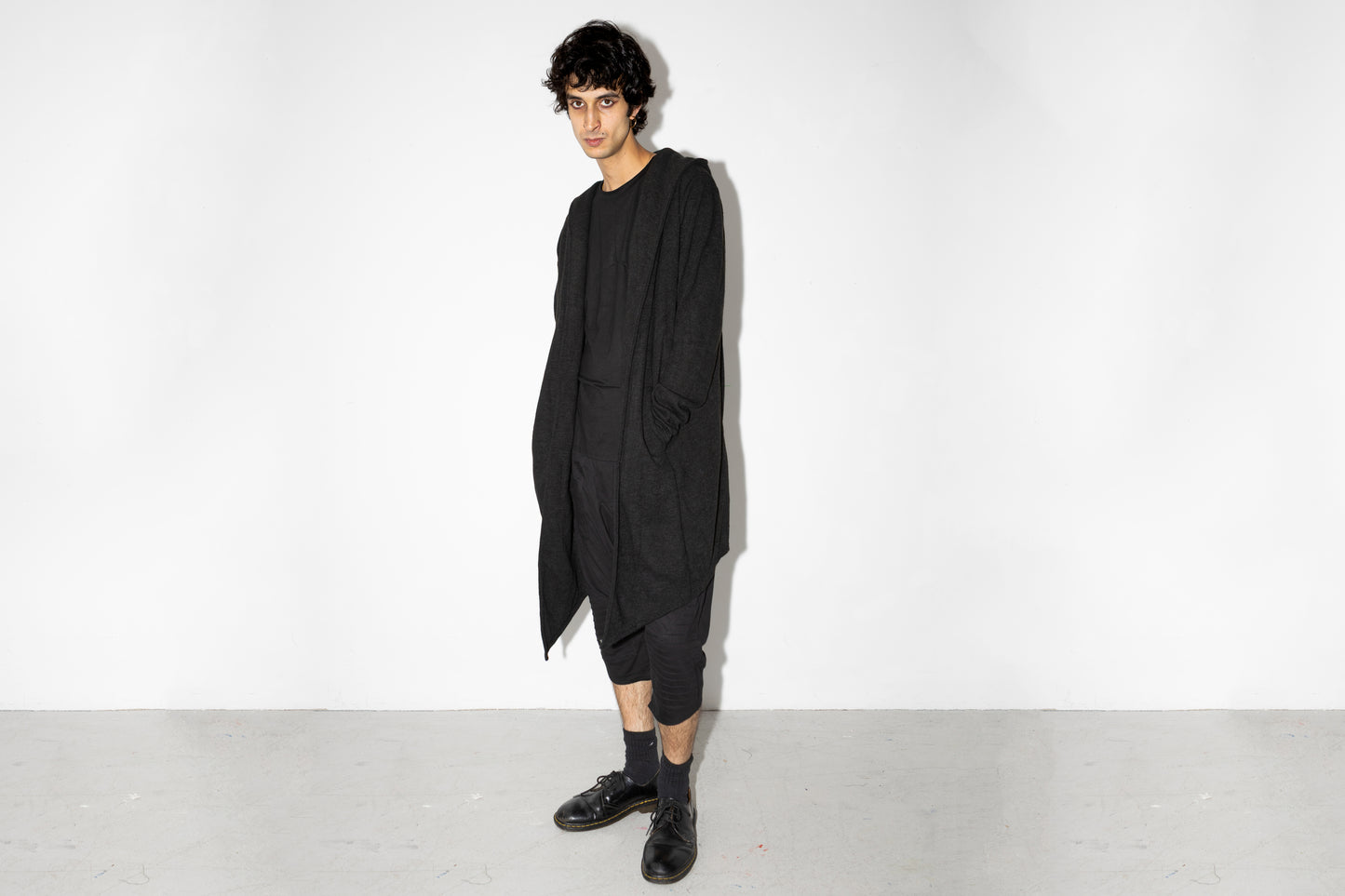 Model trägt langen schwarzen Strickmantel mit Kapuze im Dark Fashion Look.
