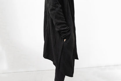 Detailansicht des schwarzen Strickmantels mit Kapuze, seitliche Tasche und strukturierte Oberfläche, Darkwear Mode mit klaren Linien.