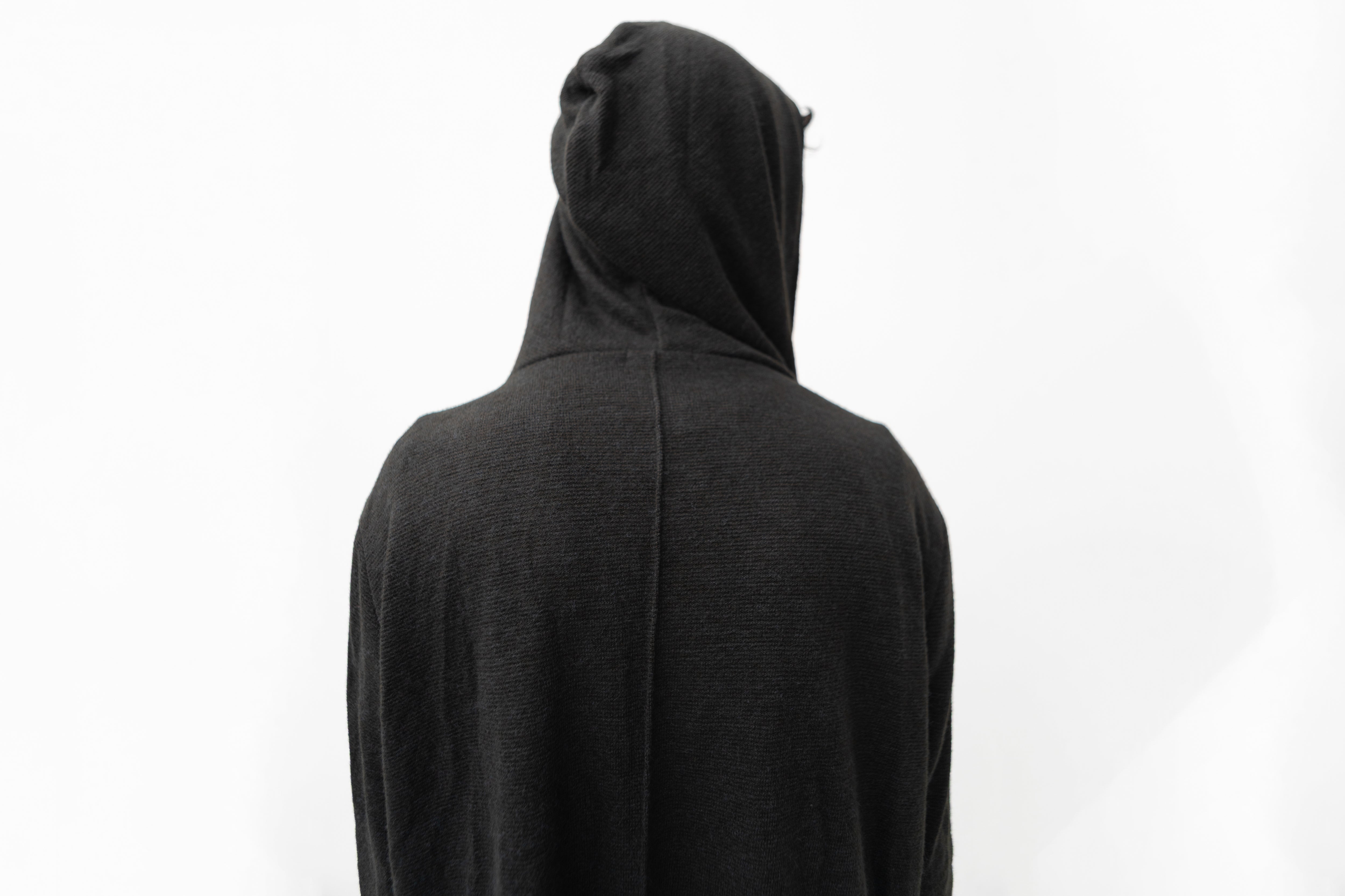 Detailansicht des schwarzen Strickmantels mit Kapuze, strukturierter Oberfläche und dekorativer Naht am Rücken.