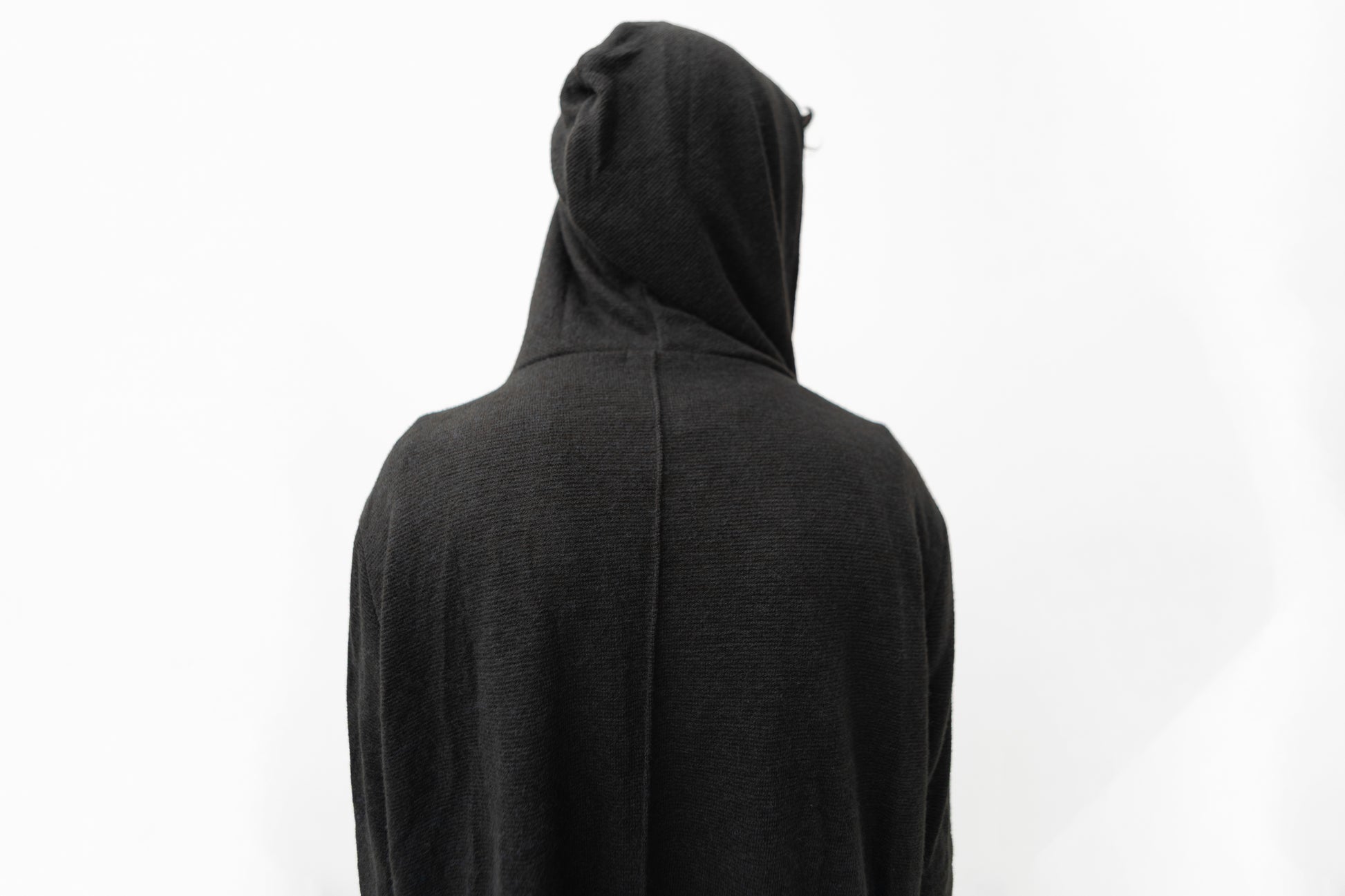 Detailansicht des schwarzen Strickmantels mit Kapuze, strukturierter Oberfläche und dekorativer Naht am Rücken.