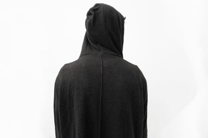 Detailansicht des schwarzen Strickmantels mit Kapuze, strukturierter Oberfläche und dekorativer Naht am Rücken.