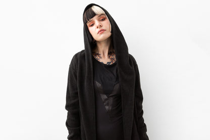 Nahaufnahme von Model mit schwarzem Kapuzenmantel im Goth- und Cyberpunk-Stil, mit extra großer Kapuze und strukturiertem Material.