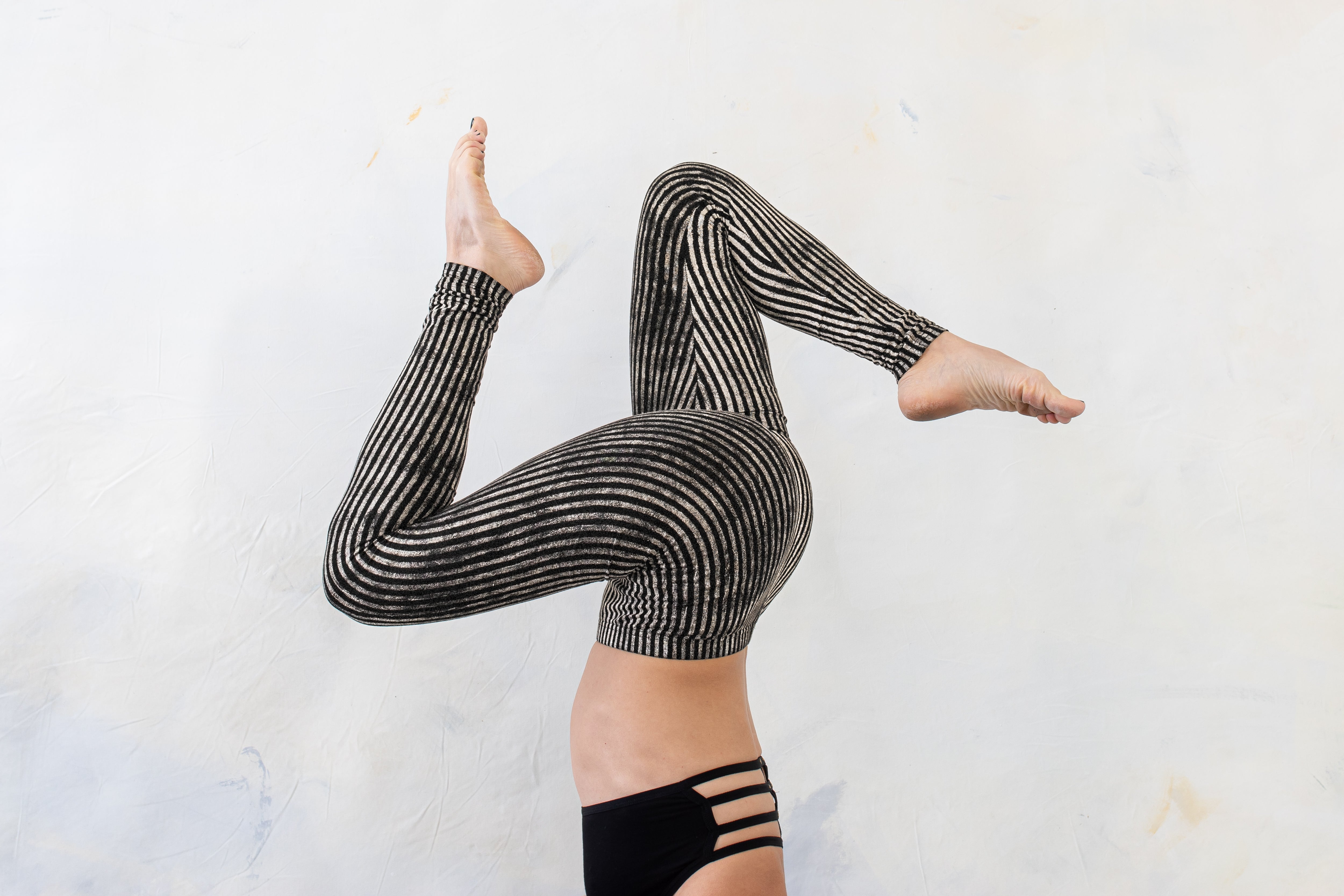 Weiblich gelesenes Model in akrobatischer Pose trägt schwarz-beige gestreifte Zirkus-Leggings.