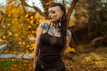 Oberkörperansicht eines tätowierten Models im Wald mit ärmellosem schwarzem Cut-out-Kleid und Bauchtasche