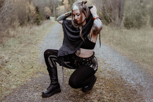 Model trägt schwarzen Riemchen-BH mit geometrischen Schnürungen, fließenden Poncho und Leggings mit abstraktem Print