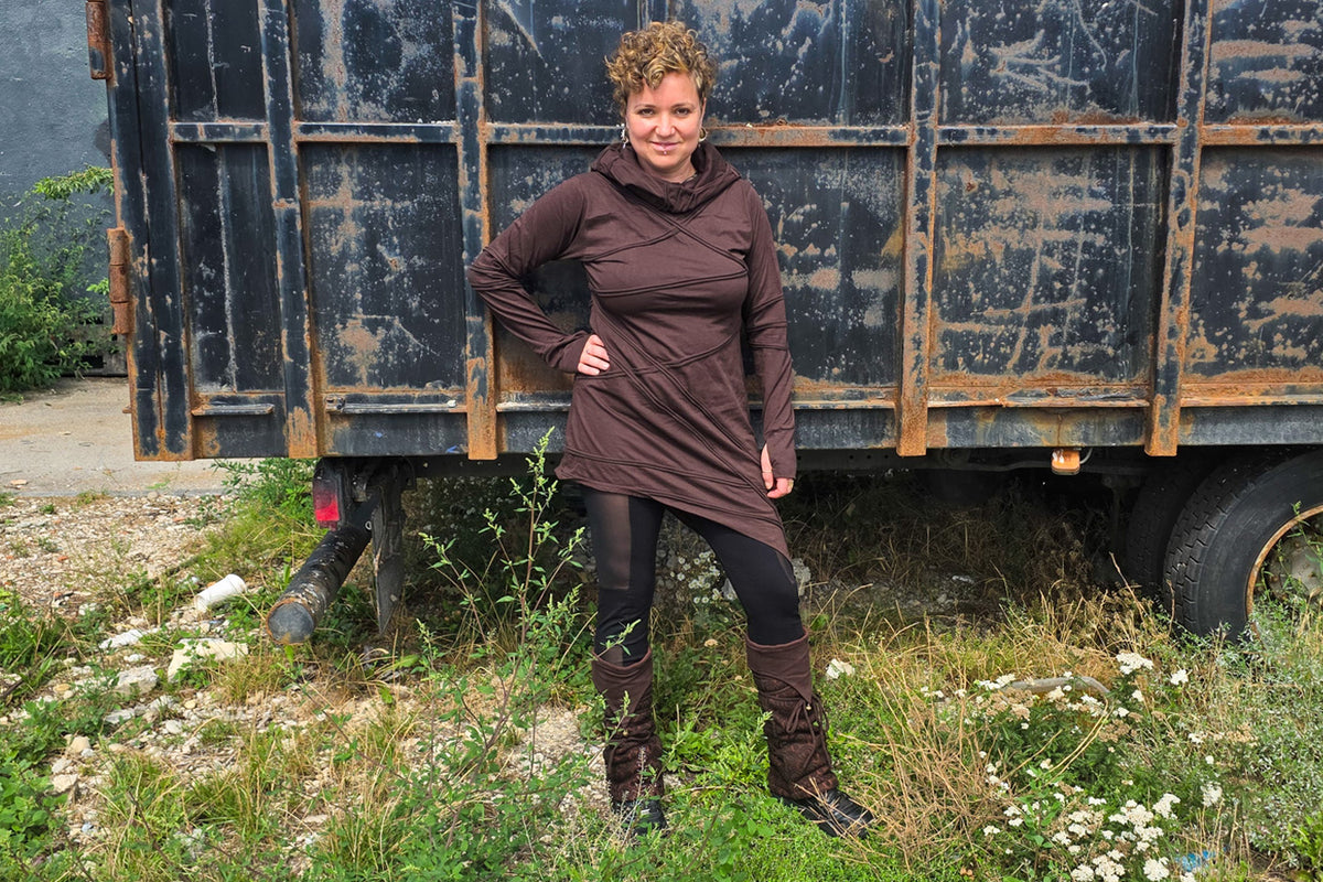 Model trägt ein braunes Langarmkleid mit großer Kapuze, Spitzen-Beinstulpen und schwarze Mesh-Leggings