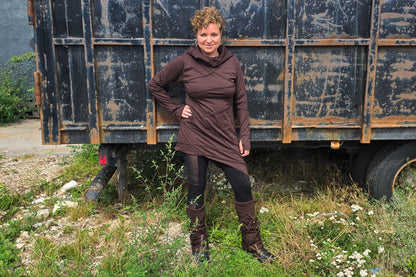 Model trägt ein braunes Langarmkleid mit großer Kapuze, Spitzen-Beinstulpen und schwarze Mesh-Leggings