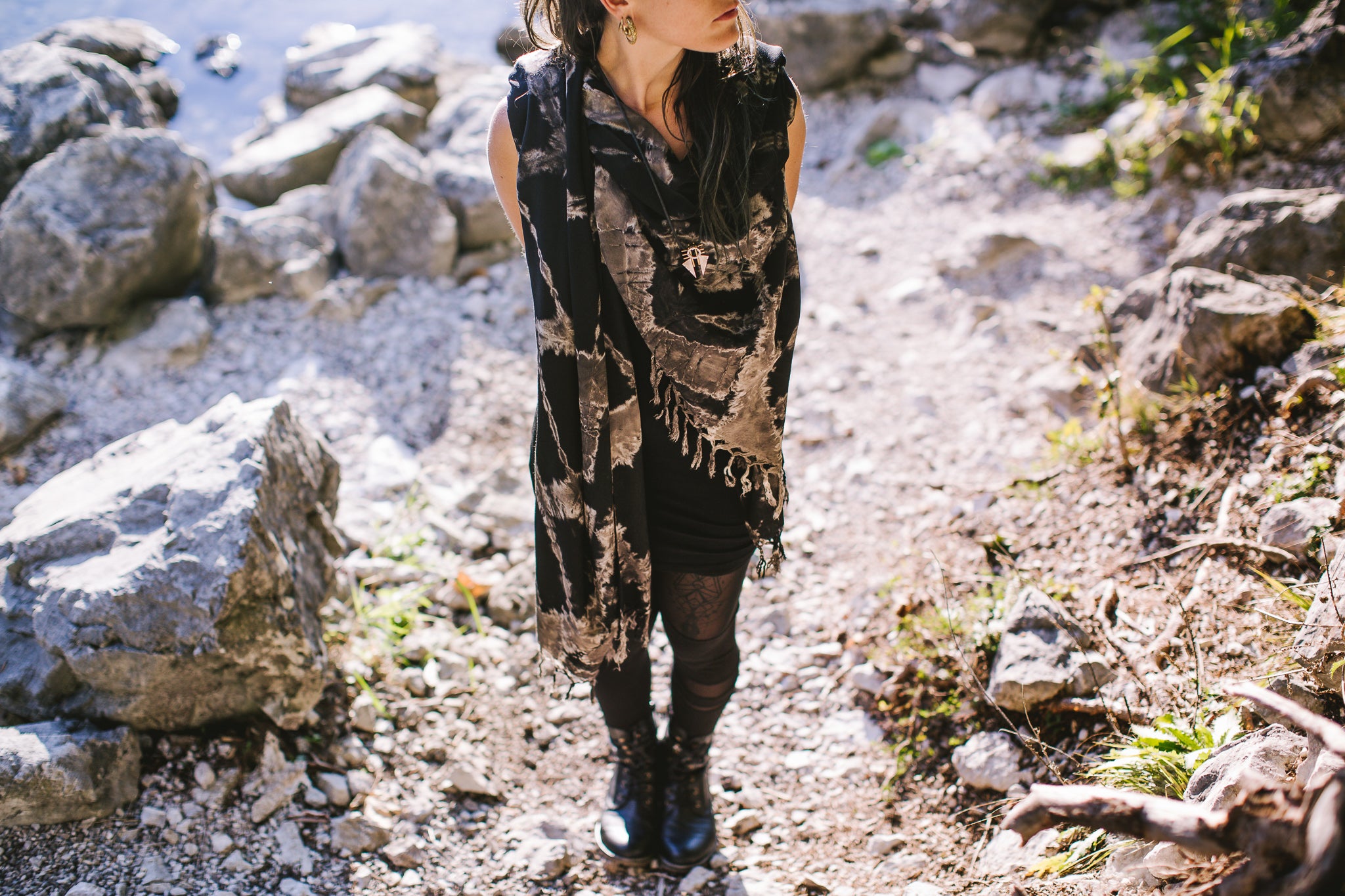 Model trägt einen schwarzen Viskose-Sarong mit beige-grauem Batik-Zick-Zack-Muster und Fransen als Schal in der Natur
