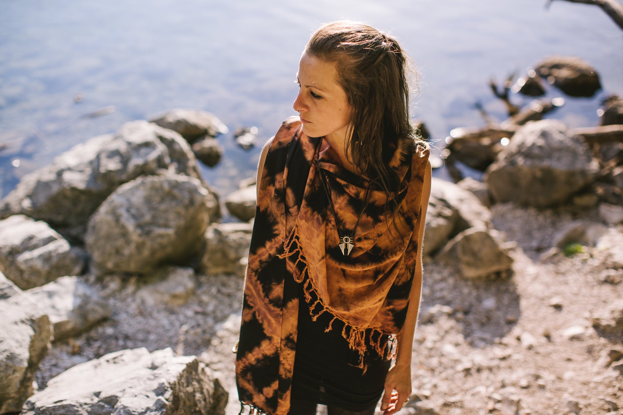 Model trägt einen schwarzen Viskose-Sarong mit orange-lila Batik-Zick-Zack-Muster und Fransen als Schal in der Natur