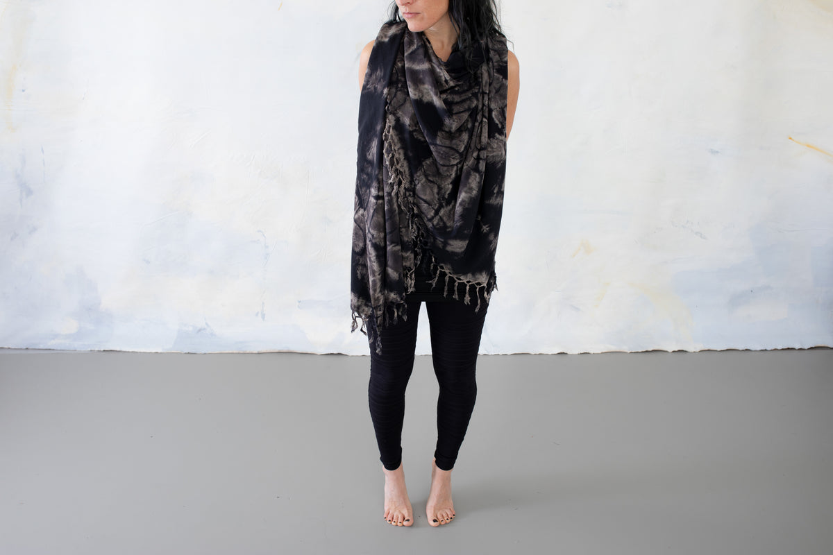 Model trägt einen schwarzen Sarong mit grau-beigem floralem Batikmuster und Fransen um Hals und Oberkörper