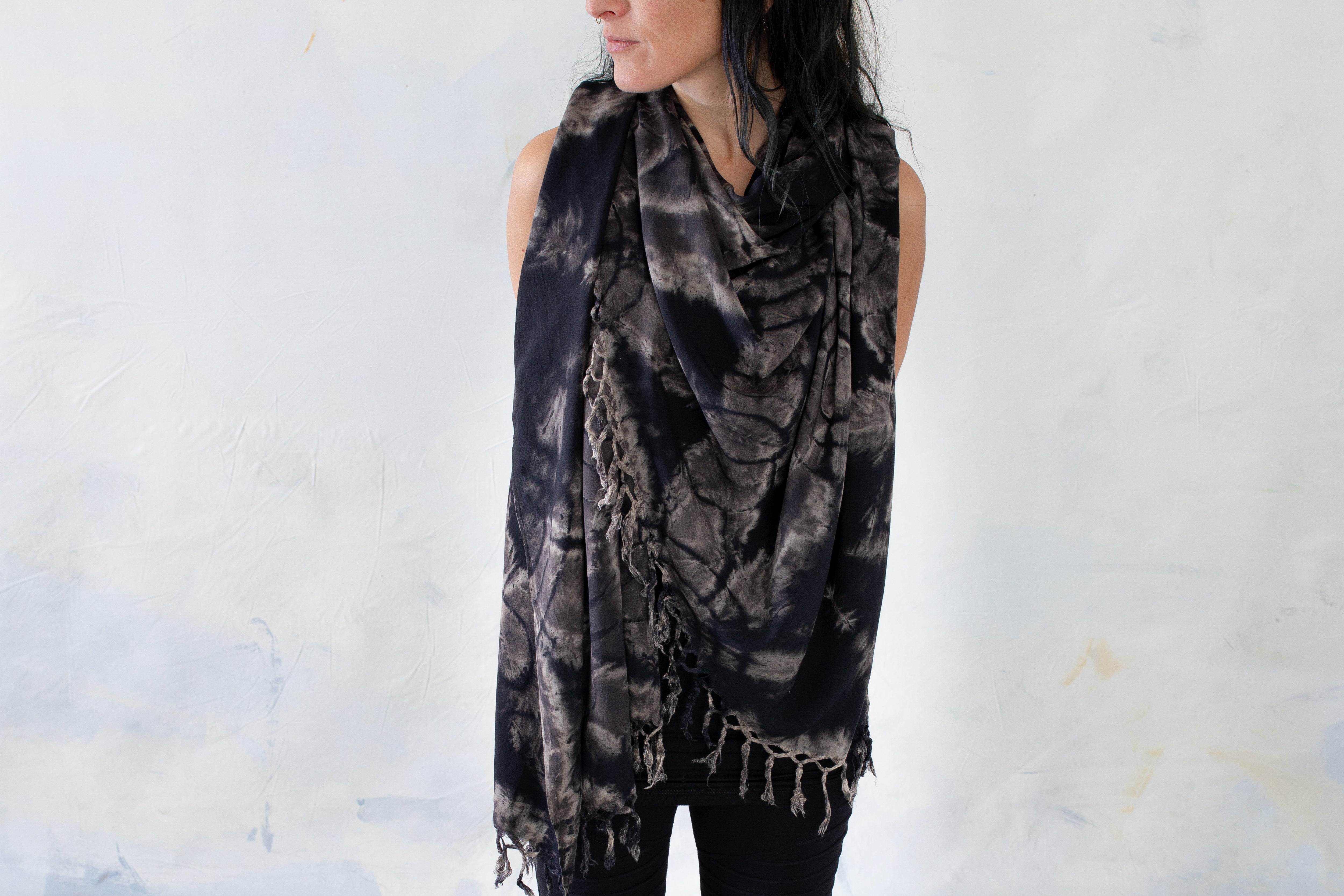 Model trägt einen schwarzen Sarong mit floralem Batikmuster in Beige- und Grautönen und Fransen als Tuch
