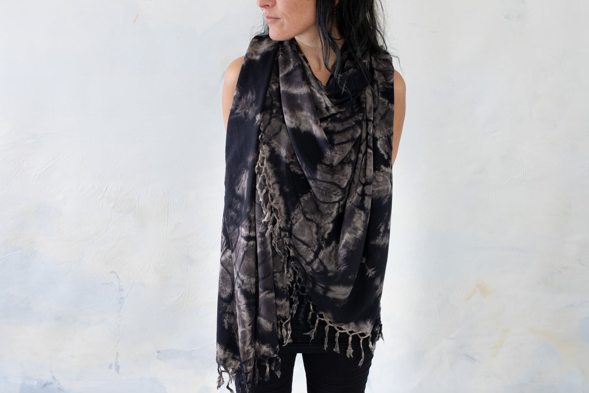Model trägt einen schwarzen Sarong mit floralem Batikmuster in Beige- und Grautönen und Fransen als Tuch