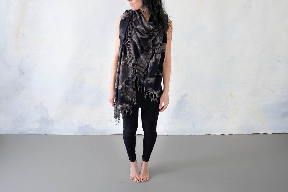 Model trägt einen schwarzen Sarong mit beige-grauem floralem Batikmuster und Fransen um Hals und Oberkörper